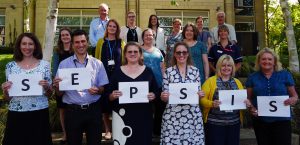 Multi-disciplinary group of health professionals holding up cards spelling out sepsis